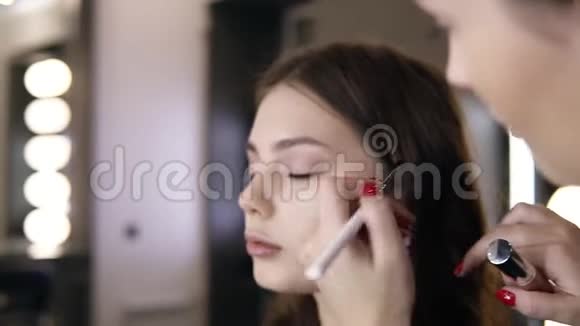 化妆师在模特的眼皮上施加最后的眼影淡妆工作室关闭录像视频的预览图