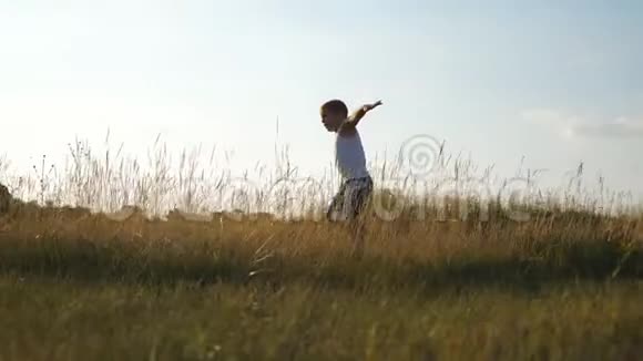 小男孩举起双手像飞机在草地上奔跑日落时分快乐的孩子在草坪上慢跑视频的预览图