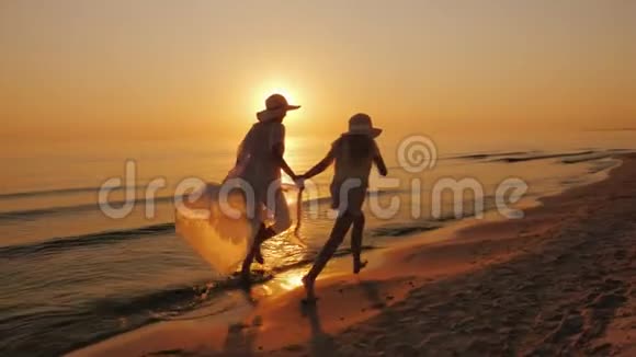 一个带着孩子的女人沿着海边的水边漫不经心地奔跑美丽的日落视频的预览图