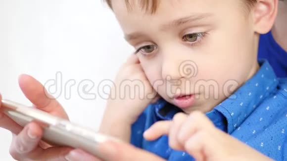 一个快乐的微笑男孩的特写肖像妈妈和宝宝玩智能手机孩子触摸到了触摸屏视频的预览图