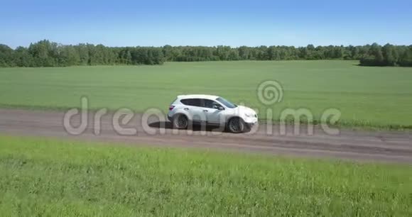 白色的汽车沿着绿色田野间的小径快速行驶视频的预览图