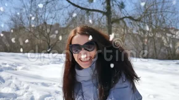 户外女画像一位年轻活跃的女士戴着深色太阳镜在公园的蓝天背景下玩雪球视频的预览图