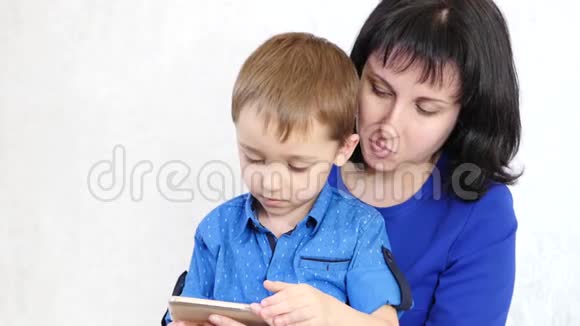 女人和孩子看着智能手机的屏幕笑妈妈和儿子玩一个发展中的游戏生活在视频的预览图