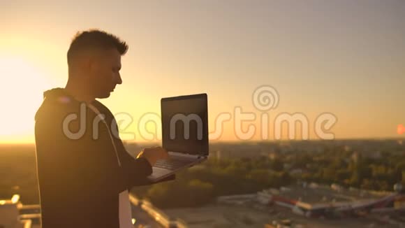 日落时分一名男性自由职业程序员坐在摩天大楼屋顶上手提电脑和键盘上的啤酒输入代码视频的预览图