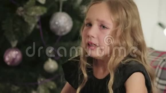 美丽的小女孩坐在圣诞树的背景下哭泣视频的预览图