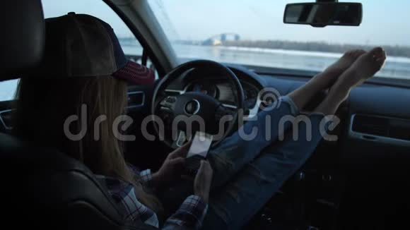 女孩坐在车里放松她写短信窗外是一道美丽的风景河和桥4K慢视频的预览图