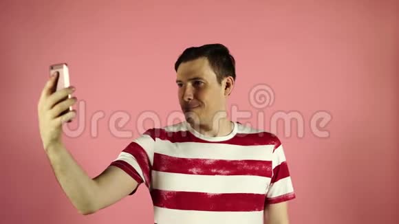 一个开朗英俊的年轻人站在粉红色背景下的手机上自拍的肖像视频的预览图