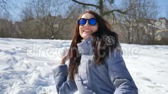 穿着蓝色镜子太阳镜和黑色直发的漂亮女孩在户外玩雪球视频的预览图