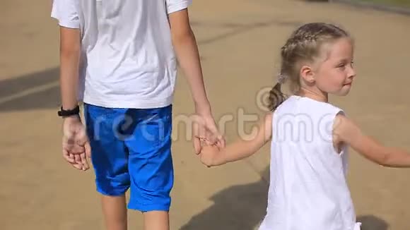 姐姐牵着哥哥的手孩子们在阳光明媚的一天走在海边快乐的童年视频的预览图