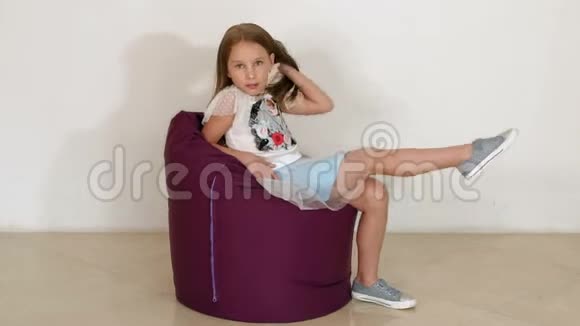 可爱的小女孩坐在紫豆袋沙发上作为客厅慢动作视频的预览图