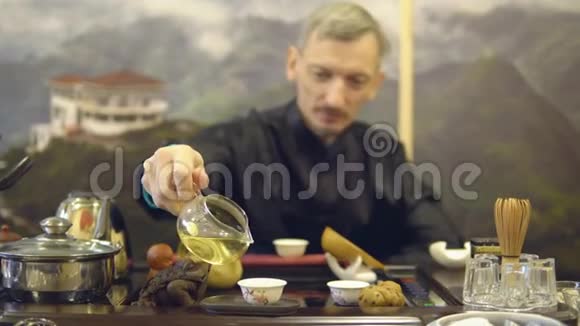 茶道主人把绿茶从玻璃茶壶倒入白色杯子里视频的预览图
