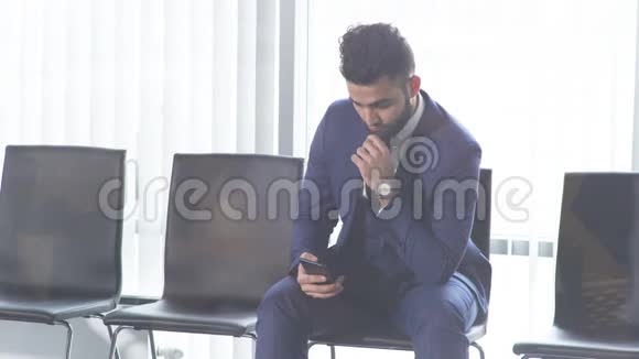 穿着时尚西装坐在智能手机旁的寂寞帅哥视频的预览图