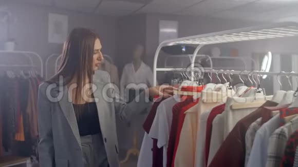 一个年轻的布鲁内特在一家服装店选择一件连衣裙挂在一个衣架上在店里买件衣服视频的预览图