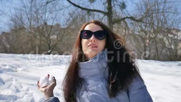 户外女画像美丽的成年女孩戴着深色太阳镜在公园的蓝天背景下玩雪球视频的预览图