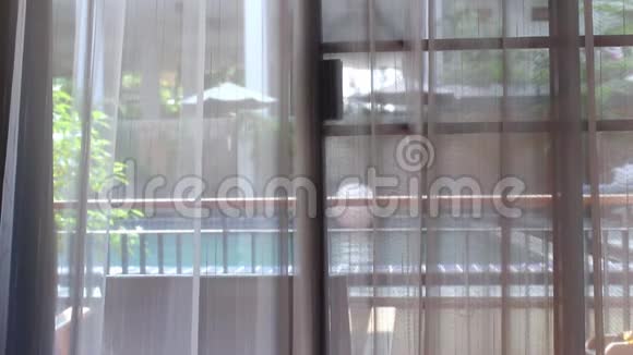 打开白色窗帘从房间的阳台上看到游泳池的景色在度假村度暑假的一天放松的椅子上视频的预览图