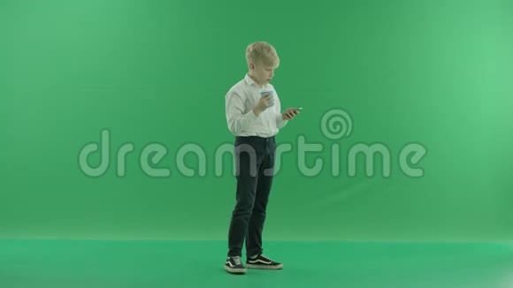 一个穿着校服的金发小男孩正拿着一杯咖啡或茶用手机说话他站着视频的预览图