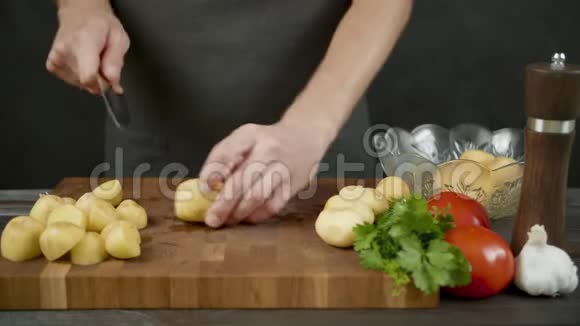 男人在厨房黑色背景的木切割板上切土豆视频的预览图