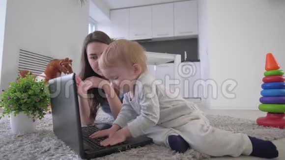 现代的童年快乐的学步男孩与年轻的母亲按下按钮笔记本电脑和拍手躺在地板上视频的预览图