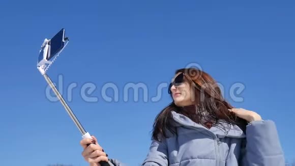 神奇的成年女孩戴着深色太阳镜一边在公园里用智能手机和棍子在户外自拍一边摆姿势视频的预览图