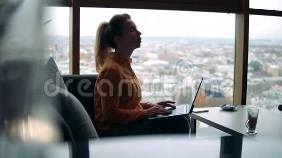 一个有电脑的女人正在一家有城市景色的咖啡馆工作视频的预览图