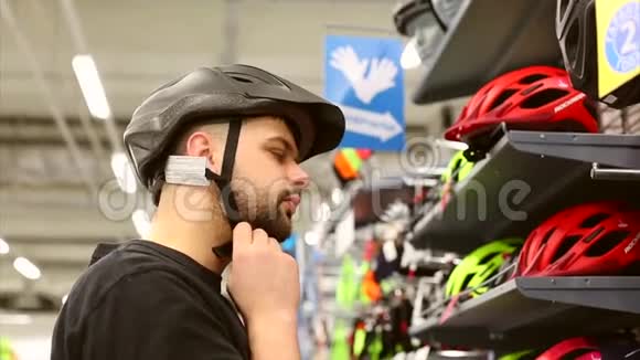 一个年轻人站在自行车商店的一个看台附近在小商店里选择自行车头盔视频的预览图