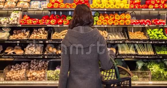 一个年轻的黑发女人站在杂货店一排农产品前面的移动框架视频的预览图