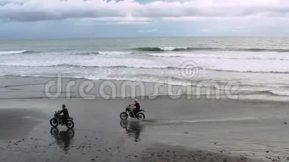 两个英俊的嬉皮士男子骑着现代定制摩托车咖啡馆赛车在黑色沙滩附近的海洋冒险视频的预览图