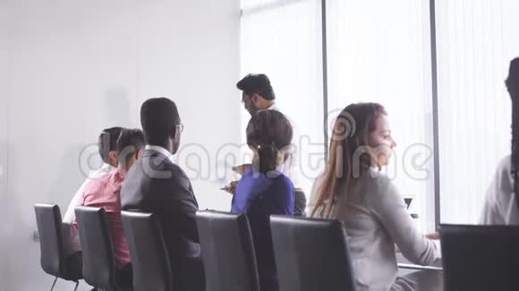 混合种族的人坐在会议室的桌子旁听演讲视频的预览图