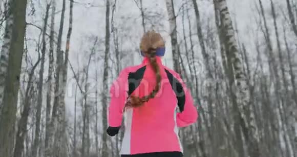 冬天一个年轻的女人穿着一件粉红色的夹克穿过公园从后面看视频的预览图