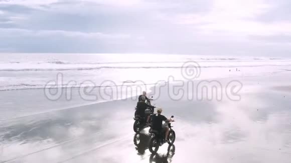 三个英俊的嬉皮士男子骑着现代定制摩托车咖啡馆赛车在黑色沙滩附近的海洋冒险视频的预览图