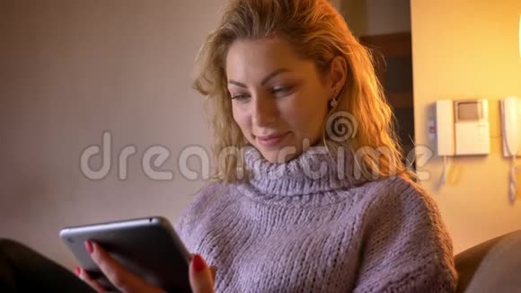 在平板电脑上浏览白种人成年金发女性的特写镜头并兴高采烈地微笑着看着室内镜头视频的预览图