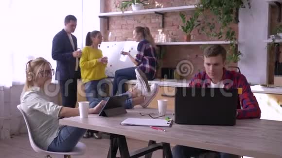 一群成功的年轻上班族正在厨房里用平板电脑和笔记本电脑吃饭和工作视频的预览图