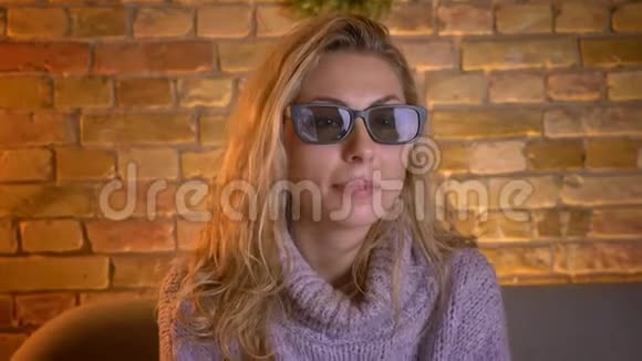 成年白种人金发女性用3D眼镜在电视上观看3D电影坐着享受乐趣的特写镜头视频的预览图