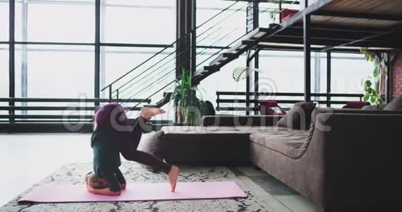 有魅力的运动女士在家里练习瑜伽在客厅的垫子上她做瑜伽姿势倒立视频的预览图
