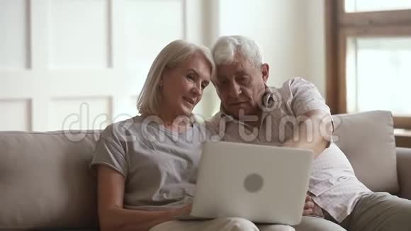 幸福的老夫妇用笔记本电脑坐在沙发上聊天视频的预览图