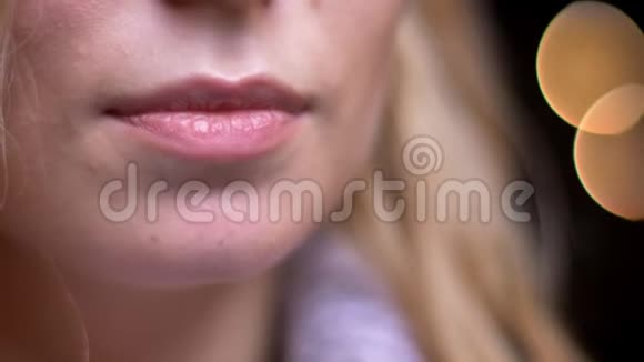 成年金发白种人女性嘴唇的特写镜头背景上的bokeh灯光诱人地微笑视频的预览图