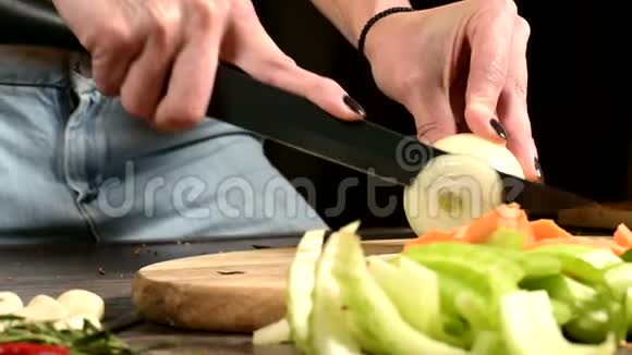 女性厨师的特写双手在切菜片旁边的木切割板上切洋葱的概念视频的预览图
