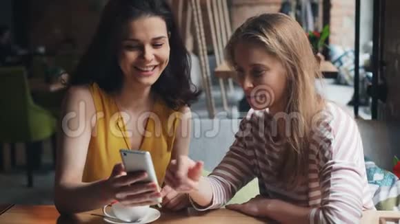 快乐的朋友们在咖啡馆里看着智能手机屏幕谈笑风生视频的预览图