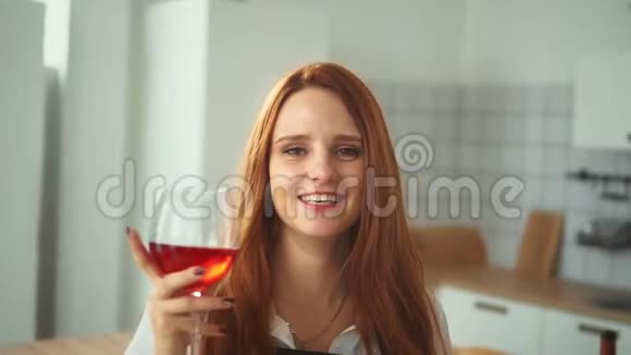 家庭厨房里带酒杯的微笑女人红头姑娘视频的预览图