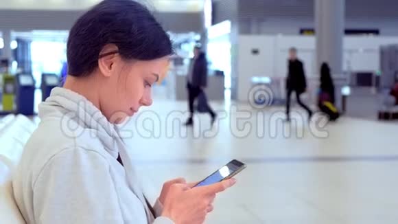 机场的女人手里拿着手机发短信等待她的航班侧视视频的预览图