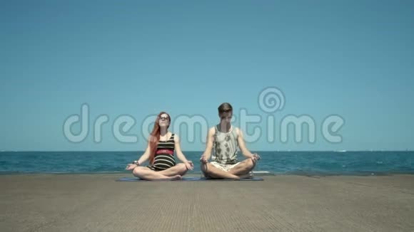 年轻夫妇坐在海边的码头上沉思带瑜伽课的假期视频的预览图