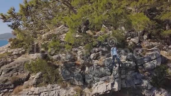 海边岩石峭壁上年轻旅行者的鸟瞰图视频的预览图