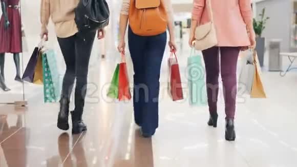 女人的后景穿着牛仔裤在购物中心散步女孩们拿着鲜艳的纸袋购物视频的预览图