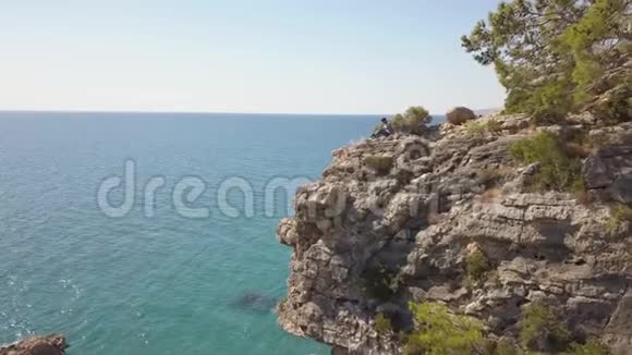 海边岩石峭壁上年轻旅行者的鸟瞰图视频的预览图