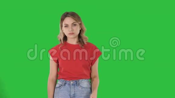 年轻的女人一头金发穿着红色t恤在绿色屏幕上毫无感情地看着摄像机彩色钥匙视频的预览图
