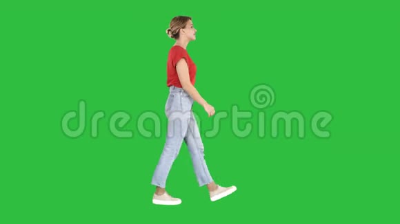 穿红色T恤牛仔裤和运动鞋的女人走在绿色屏幕上Chroma键视频的预览图
