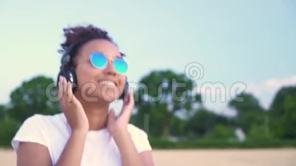 穿着白色T恤和蓝色太阳镜的女青少年在无线耳机上听音乐视频的预览图