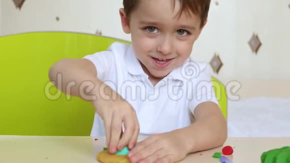 可爱的小男孩坐在桌边玩橡皮泥一个快乐有趣的孩子从一个模型组合中塑造出创造力视频的预览图