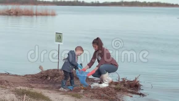拯救地球年轻的母亲和儿子志愿者从河堤附近的水中清理污染的海滩视频的预览图