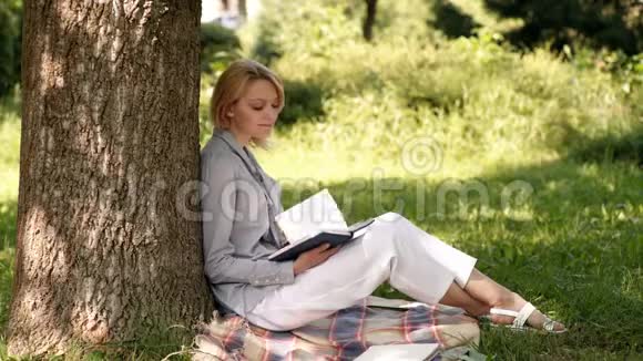 美丽的金发女孩在公园看书的肖像快乐学生轻松户外阅读画像视频的预览图